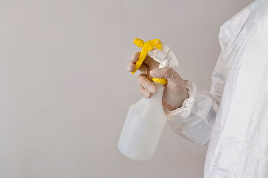 A person wearing beige cleaning gloves is adjusting or placing a lightbox sign on a table, which displays the words 'CLEANING HOME' in bold capital letters. The background is a softly lit, modern inte